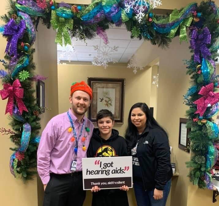 Audiologist with woman and son holding a sign that says "I got hearing aids."