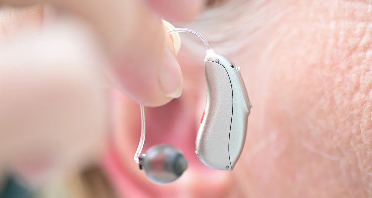 Silver hearing aid being held up with two fingers